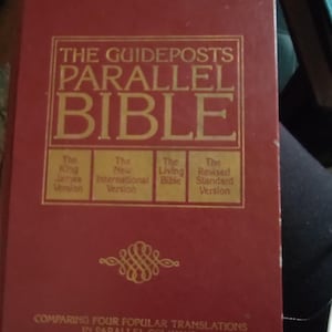 May include: A red hardcover book titled "THE GUIDEPOSTS PARALLEL BIBLE" with gold lettering. The book compares four popular translations in parallel columns. The cover features the King James Version, New International Version, The Living Bible, and Revised Standard Version.