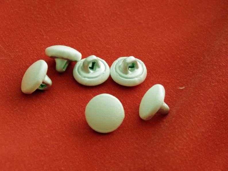 May include: Six white plastic buttons with a silver metal shank. The buttons are round and have a smooth surface.