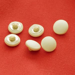 May include: Six white plastic buttons with a silver ring around the center. The buttons have a raised center and are arranged on a red surface.
