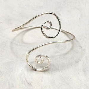 May include: Silver wire bracelet with two spiral designs. The bracelet is open and adjustable.