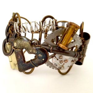 May include: A steampunk-style bracelet made of metal and wire. It features a heart-shaped charm, a key, a gear, and a small glass vial. The bracelet is a unique and stylish accessory.