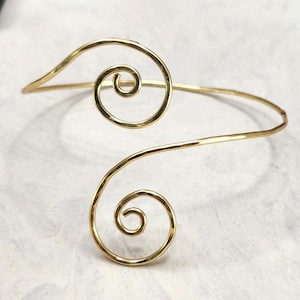 May include: A gold-toned metal cuff bracelet with two spiral designs. The bracelet is open and adjustable.
