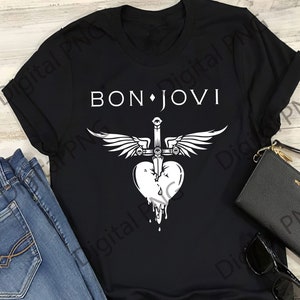 Puede incluir: Camiseta negra con el texto "BON JOVI" sobre un gráfico de un corazón atravesado por una espada con alas. El corazón tiene un efecto de goteo. La camiseta se muestra con vaqueros azules, una cartera negra y gafas de sol.