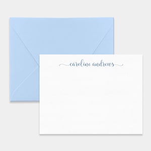 May include: A white rectangular stationery card featuring the name caroline andrews printed in a dark blue cursive script font, accompanied by a matching light blue envelope positioned behind the card with the flap facing upward.