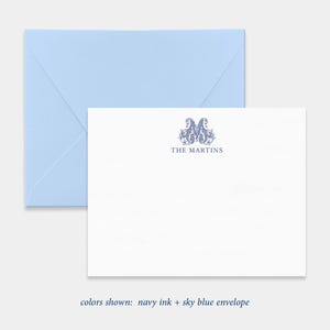 May include: A white stationery card featuring a navy blue ornate monogram letter M and the text THE MARTINS centered below it, paired with a light sky blue envelope. The card displays navy ink and a sky blue envelope color scheme.