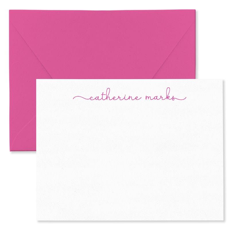 May include: A white stationery card with the name "catherine marks" in pink script, accompanied by a bright pink envelope. The card and envelope are set against a white background.