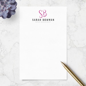 May include: A white rectangular sheet of paper featuring a pink cursive SB monogram logo above the black text SARAH BOWMAN and the smaller text BRAND MANAGEMENT, accompanied by a gold pen resting on the bottom right corner of the paper.