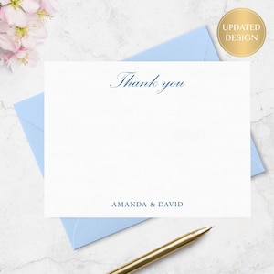 May include: A white thank you card with the words "Thank you" in elegant navy blue script. The card is on a light blue envelope, with the names "AMANDA & DAVID" printed at the bottom. A gold pen rests on the envelope.