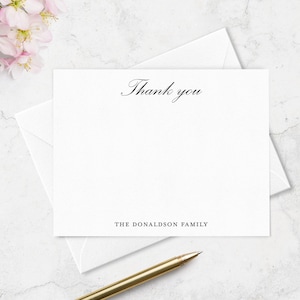 May include: A white rectangular folded note card with a matching envelope. The card features the text Thank you in a black script font at the top and the text THE DONALDSON FAMILY in a black sans-serif font at the bottom center of the card.