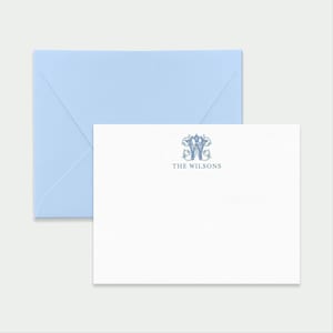May include: A white rectangular stationery card featuring a dark blue ornate letter W monogram and the text THE WILSONS centered below it, accompanied by a light blue envelope positioned behind the card.