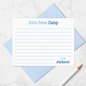 May include: A white rectangular stationery card with light blue and dark blue horizontal lines. The text reads Hello from Camp at the top and from Jackson at the bottom right. The card is placed on a light blue envelope with a white pencil nearby.