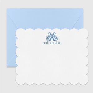 May include: A white scalloped-edge note card featuring a blue ornate monogram of the letter M and the text THE MILLERS printed in blue, paired with a light blue envelope. The stationery set displays a clean design with a textured paper finish.