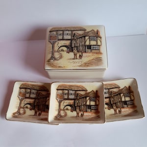 May include: A set of three ceramic trinket dishes and a matching box featuring a vintage illustration of a building with the text "The Jolly Miller" on a sign. The dishes and box are cream coloured with gold trim.