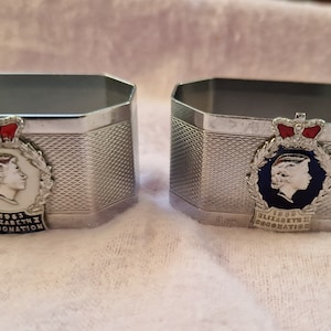Puede incluir: Dos anillos de servilleta de plata con un diseño en relieve que presenta un perfil de la reina Isabel II y el texto "1953 ELIZABETH II CORONATION".