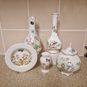 以下が含まれることがあります： 花柄と蝶の模様が施された白い磁器製の壺とボウル5点セット。壺はカラフルな花と蝶で飾られており、ボウルは青い蝶がついた花柄です。