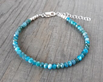 May include: A delicate bracelet featuring small, faceted blue-green beads strung together. The bracelet has a silver-colored clasp and an adjustable chain. The beads are a mix of light and dark shades of blue and green.