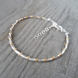 May include: A silver and gold bracelet with a chain clasp. The bracelet is made of small, rectangular beads.