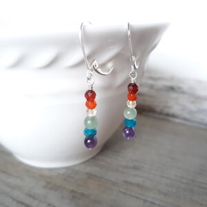 May include: Silver dangle earrings with seven gemstone beads in a rainbow colour sequence: red, orange, yellow, green, blue, indigo, and violet.