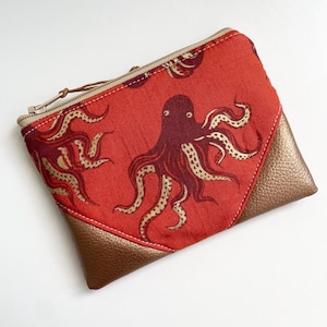 Peut inclure: Une pochette zippée rouge avec un imprimé d'octopus doré et un fond en cuir marron.