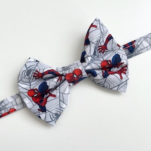 Peut inclure: Un nœud papillon gris avec un motif Spider-Man. Le tissu présente un motif répété de personnages de Spider-Man en rouge et bleu, sur un fond en forme de toile d'araignée. Le nœud papillon est en tissu.