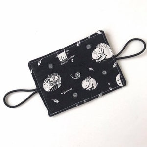May include: Black fabric pouch with a white elastic strap. The pouch has a white and black print of woodland animals, including a fox, a bear, and a rabbit.