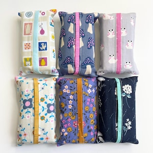 May include: Six rectangular fabric tissue covers arranged in two rows. The top row features a postage stamp print, a blue mushroom pattern with a pink centre strip, and a grey frog print. The bottom row shows a floral pattern, a purple wildflower print, and a dark blue floral design.
