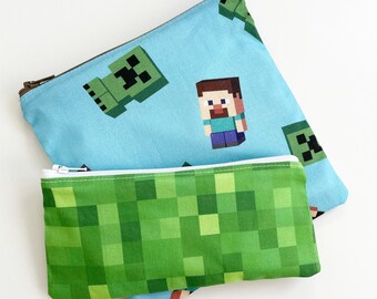 May include: Two zippered pouches, one blue with a green creeper and a pixelated character, the other green with a pixelated pattern.