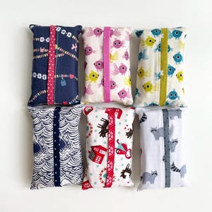 May include: Six rectangular fabric tissue holders with diverse patterns. Designs include fish, raccoons, houses, and abstract shapes. Each holder has a contrasting vertical stripe down the centre. Some holders have text.