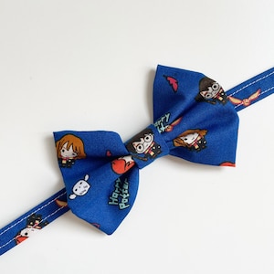 May include: Blue bow tie with a Harry Potter theme. The bow tie features a repeating pattern of Harry Potter characters, including Harry, Ron, and Hermione. The text "Harry Potter" is also visible on the bow tie.