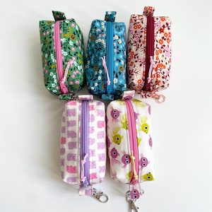May include: Six fabric pencil cases with zip closures. The cases display floral and patterned designs in green, blue, and orange. Two cases have animal prints in pink and purple, and white and yellow.