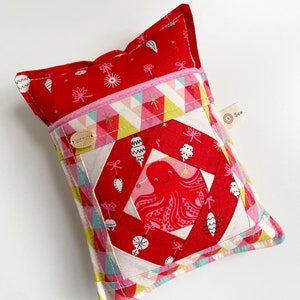 May include: Red and white quilted pillow with a pink octopus design in the center. The pillow has a small pocket on the front with a "Sew" label.