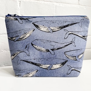 以下が含まれることがあります： クジラのプリントデザインが施された青いジッパー付きポーチ。クジラは黒と白で、ポーチ全体に繰り返しデザインされています。