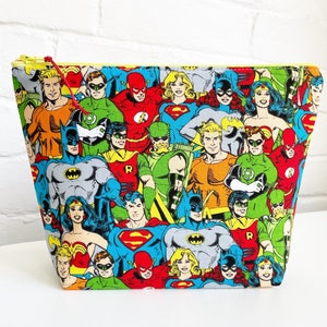 May include: A colorful zippered pouch with a pattern of various superheroes, including Superman, Batman, Wonder Woman, and The Flash.