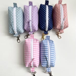 May include: A selection of small, rectangular pouches in assorted colours and patterns. Each pouch has a zip closure and a small loop with a metal clasp. Patterns include polka dots and gingham in shades of blue, pink, and purple.