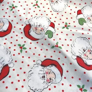 Peut inclure: Tissu blanc avec un motif répété de visages du Père Noël, de pois rouges et de brins de houx. Le Père Noël porte un bonnet et un manteau rouges, une barbe blanche et des gants verts. Un motif festif sur le thème de Noël.