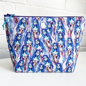 May include: A blue and white zippered pouch with a repeating pattern of a cartoon character with blue hair and a white dress.