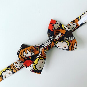 May include: A brown bow tie featuring a colourful print of cartoon characters. The characters are wearing glasses and have brown, blonde, and red hair.