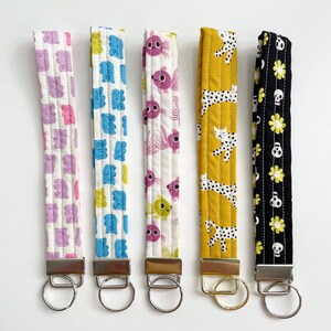 May include: Five fabric key fobs with various patterns. Designs include purple and pink gummy bears, blue gummy bears, pink fish, white cats on yellow, and black skulls with yellow flowers. Each has a metal ring.