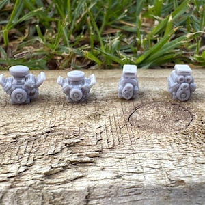 May include: A collection of six small, grey miniature engine models are displayed on a weathered wooden surface. The models showcase various engine designs. Green grass forms the background, offering a natural contrast to the industrial theme of the models.
