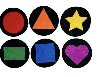 May include: Six circular black felt patches, each featuring a different colored shape centered on it: a red circle, an orange triangle, a yellow star, a green rectangle, a blue square, and a purple heart. The shapes are made of felt material.