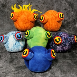 May include: Six plush toys shaped like round creatures with large eyes. The toys are in different colors, including orange, green, blue, and purple. Each toy has a unique pattern on its surface.