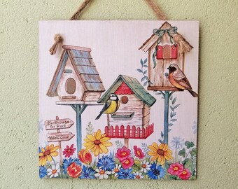 Könnte beinhalten: Ein Holzschild mit einem Vogelhaus-Motiv. Das Schild zeigt drei Vogelhäuser, zwei Vögel und ein Schild mit der Aufschrift "Birdhouse for Rent" und "Welcome". Das Schild ist mit Blumen und Grünpflanzen verziert.