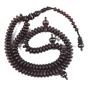 May include: A dark brown wooden prayer beads or rosary with silver accents. The beads are round and have a slightly textured surface. The beads are strung together with a thin black cord.