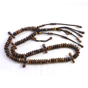 May include: A set of prayer beads made from dark brown wooden beads. The beads are strung together with black string and have decorative wooden accents. The beads are arranged in a curved pattern against a white backdrop.
