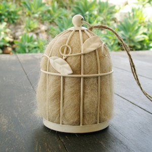 May include: A white metal birdcage with a brown, fluffy material inside. The cage has a delicate, floral design and is hanging from a string.