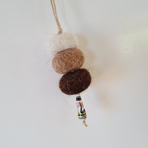 May include: A brown, beige and white felt ball ornament with a decorative ceramic bead hanging from it.