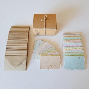 May include: A selection of stationery items, including small kraft paper envelopes, a stack of colourful handmade paper cards, and a small kraft paper box tied with twine. The box has a small illustration of a llama.