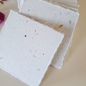 May include: A stack of white handmade paper cards with a deckled edge. The paper has a speckled texture with flecks of red, yellow, and brown.