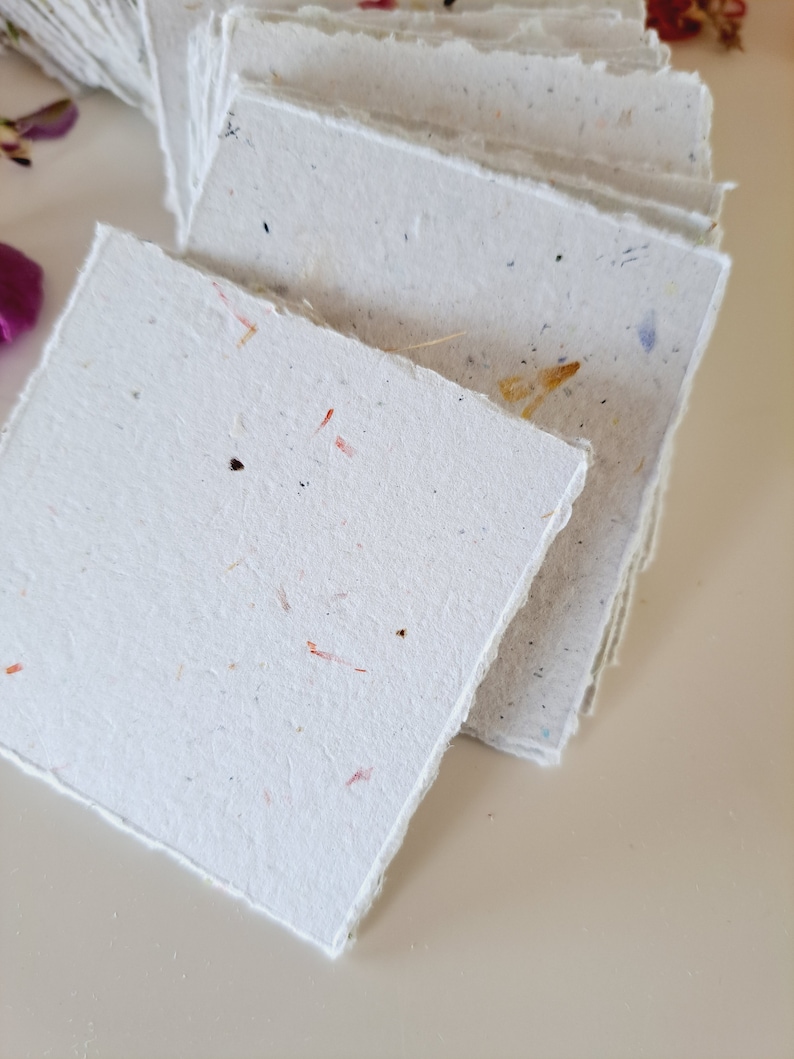 May include: A stack of white handmade paper cards with a deckled edge. The paper has a speckled texture with flecks of red, yellow, and brown.