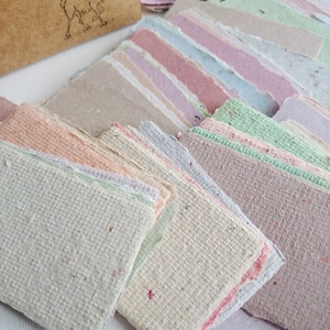 Pu&ograve; includere: Un mucchio di fogli di carta artigianale colorati con una superficie testurizzata. La carta &egrave; in varie tonalit&agrave; di rosa, blu, verde e beige.